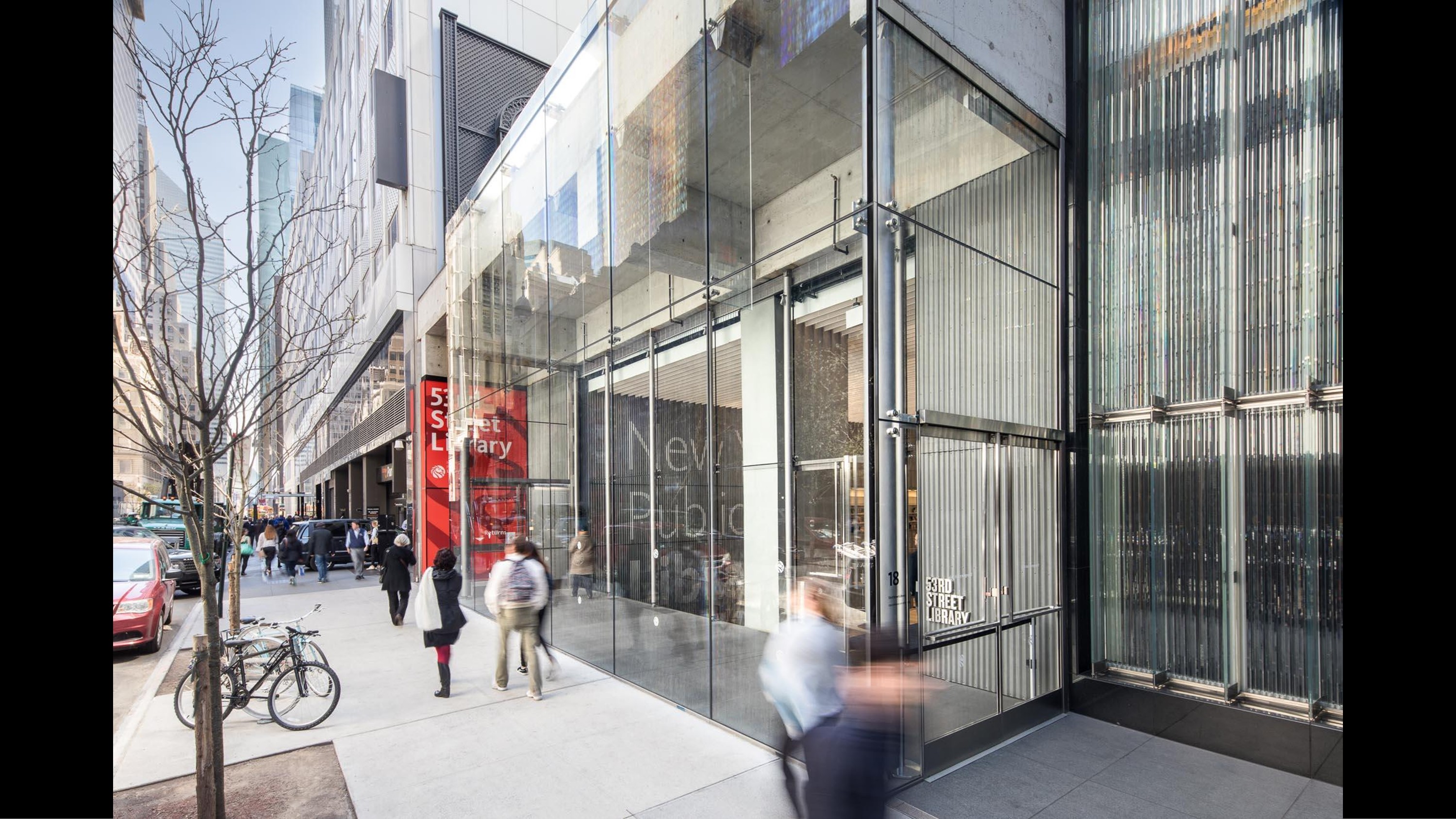 A contemporary glass facade of the 5th Street Library in an urban setting, showcasing a retail-inspired public space design with reflective surfaces and integrated brand identity.